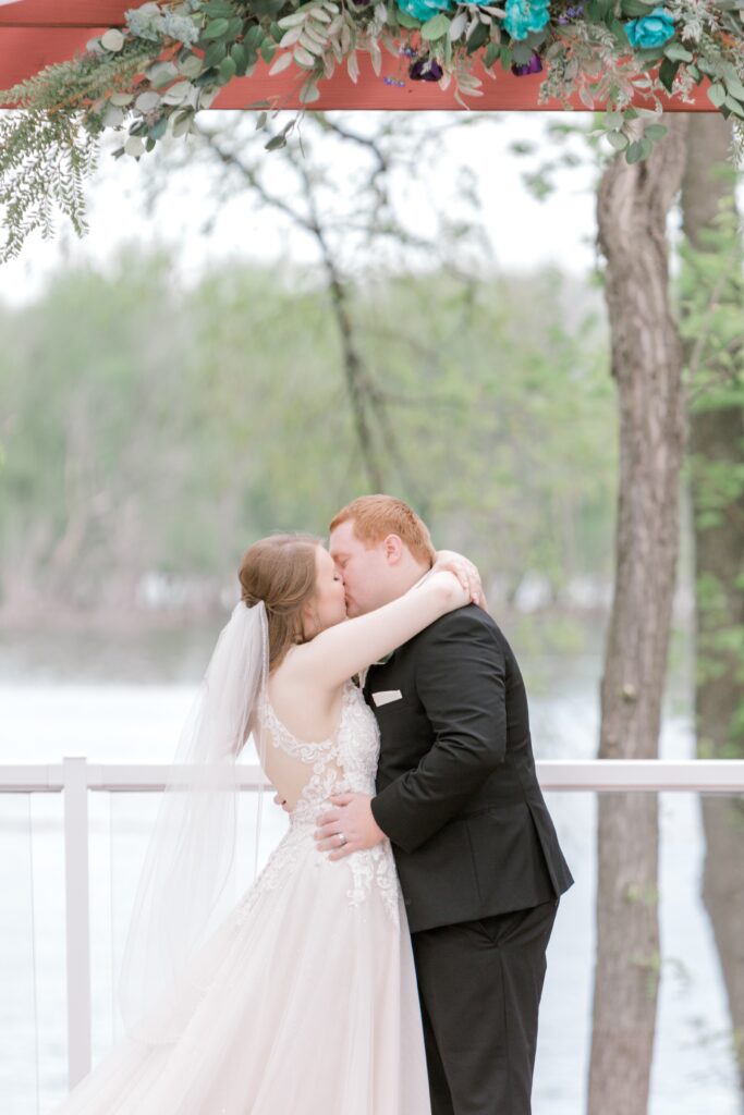 A bride and groom kissing on the side of a lake.