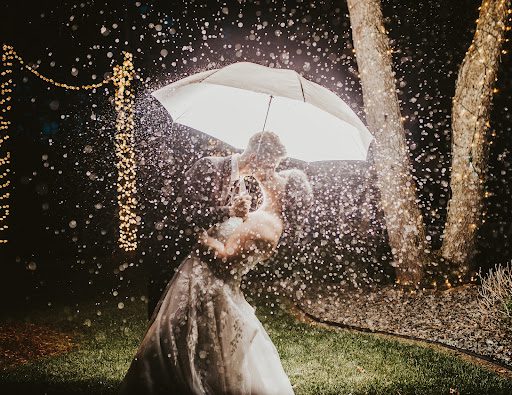 A bride and groom under an umbrella in the rain.