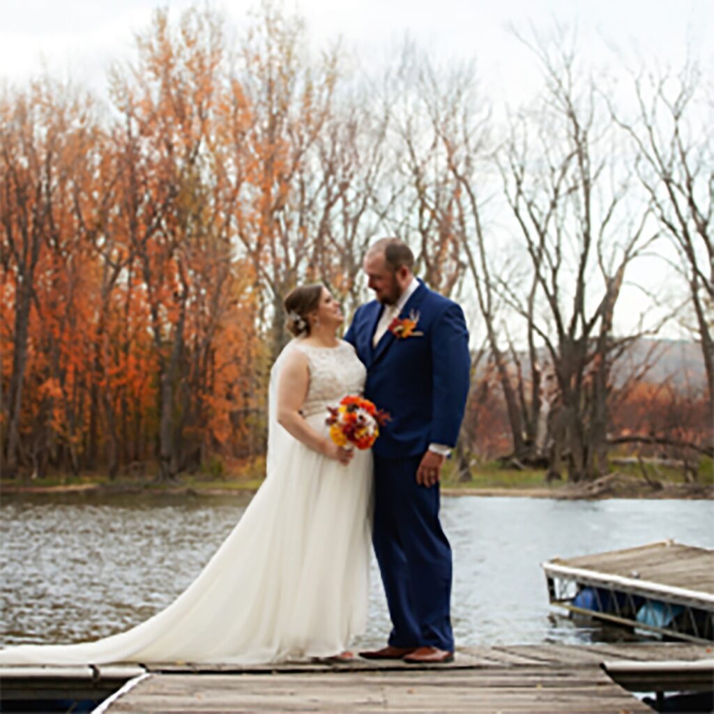 closeup photo of bride and groom standing on dock in lake