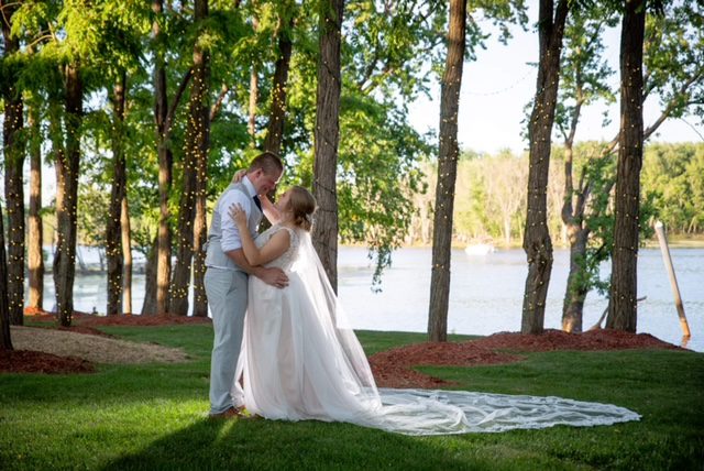 A bride and groom pose for a picture in the grass.
