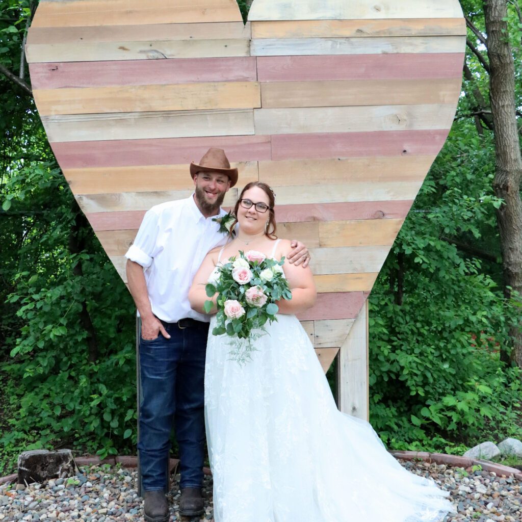 bride and groom posing in front of wooden heart