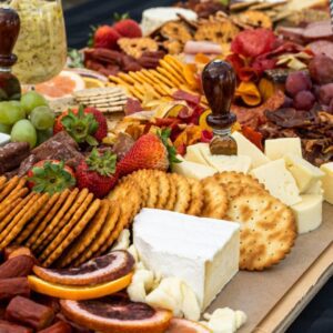 A table full of food with crackers, cheese and fruit.