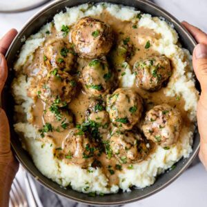 A person holding a bowl of meatballs and mashed potatoes.