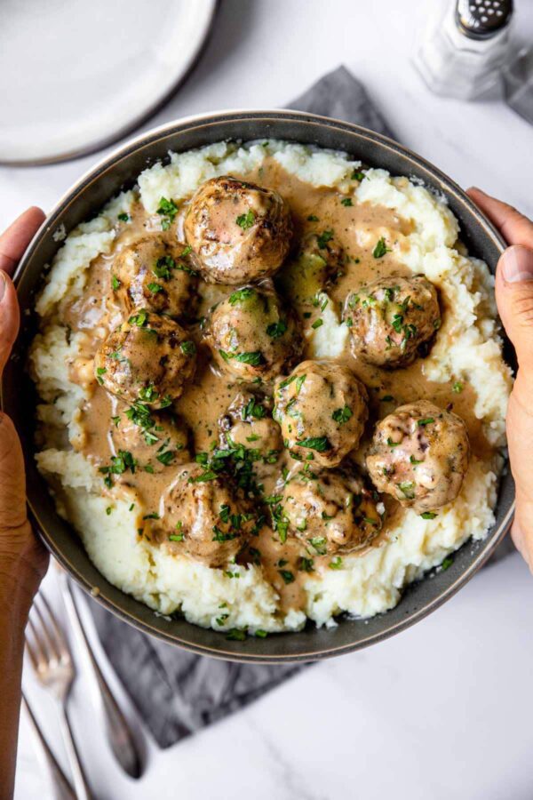 A person holding a bowl of meatballs and mashed potatoes.