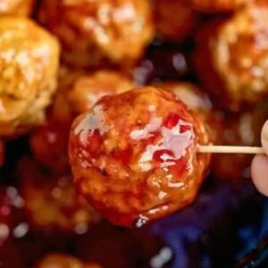 A person holding a skewer with meatballs on it.
