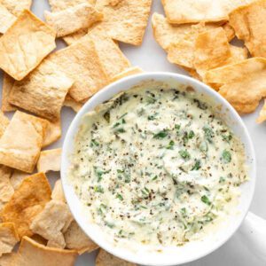 A bowl of dip next to some chips.