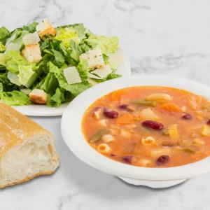 A bowl of soup, salad and bread on the table.