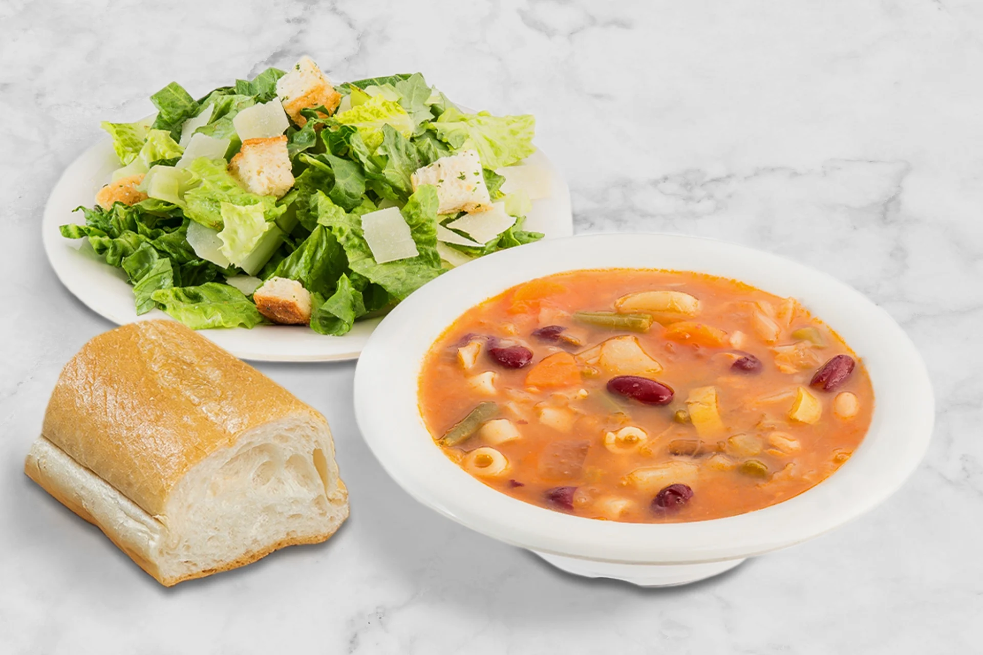 A bowl of soup, salad and bread on the table.