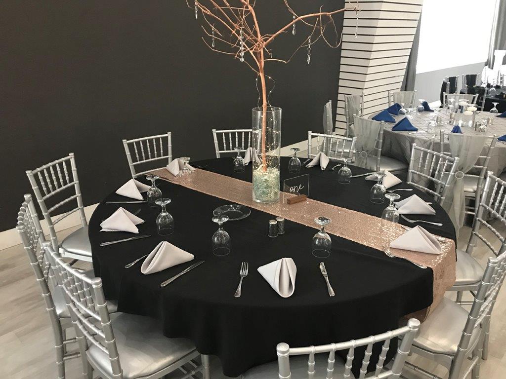 A table set up with black linens and silver chairs.