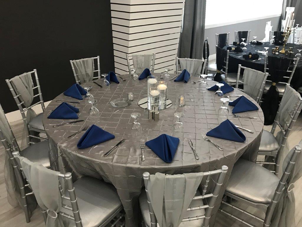 A table set with blue napkins and white chairs.