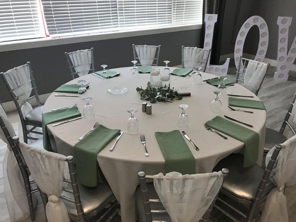 A round table with green napkins and silverware.