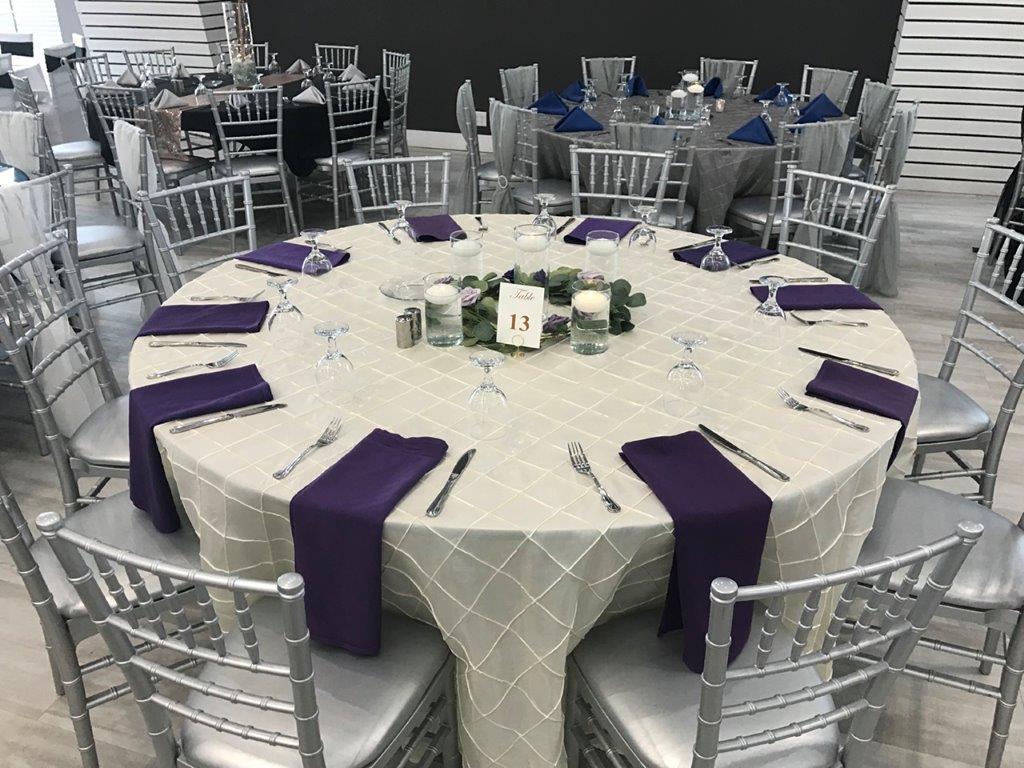 A round table with purple napkins and silver chairs.