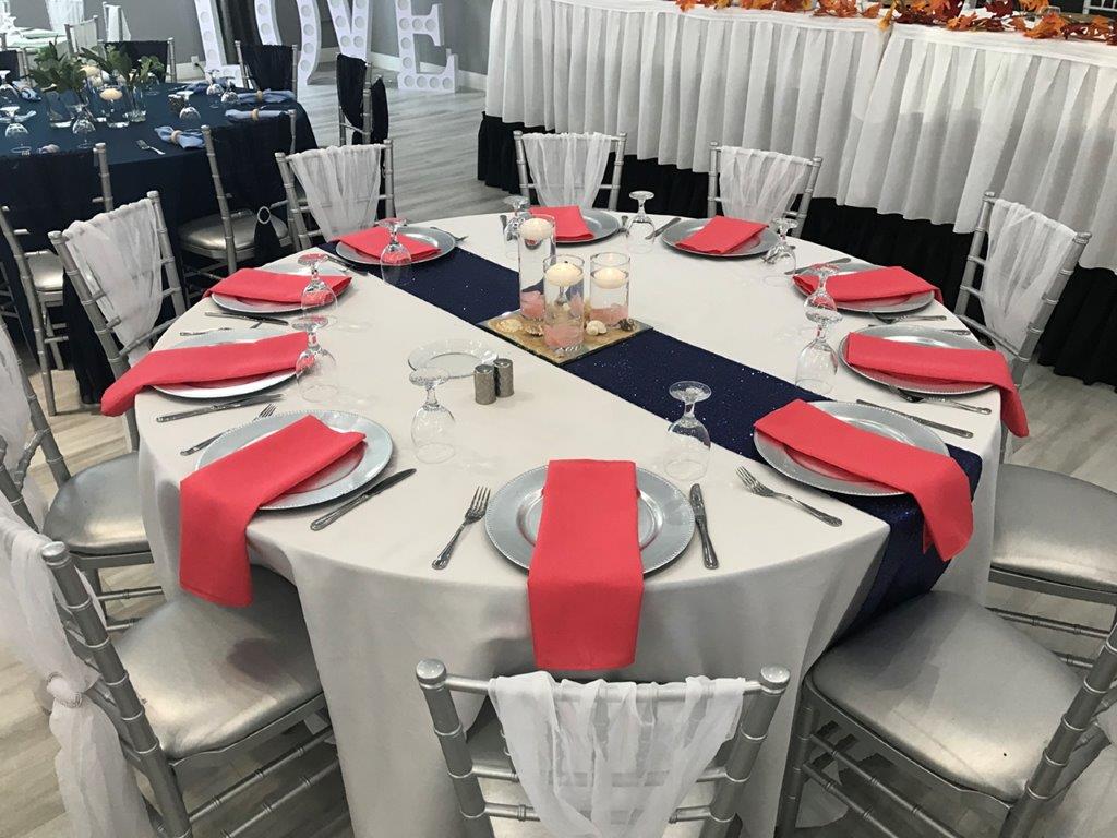 A round table with red napkins and white chairs.