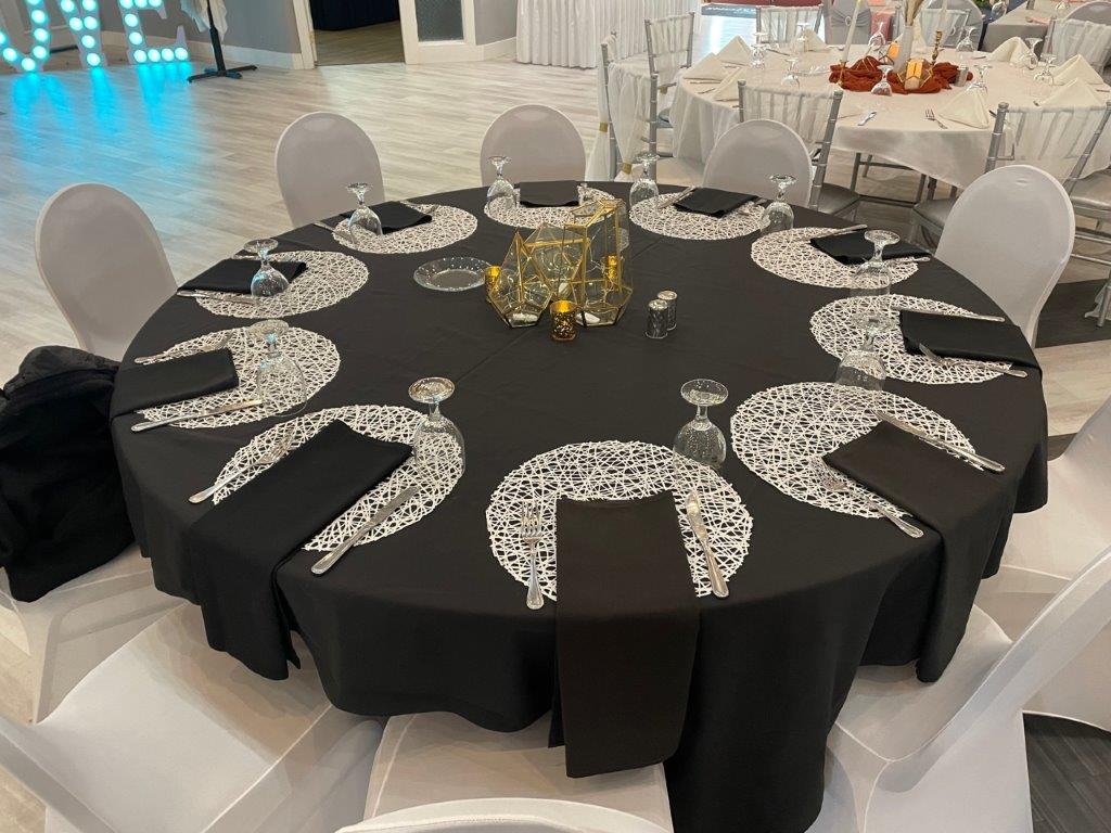 A table with black and white tablecloth, chairs and candles.