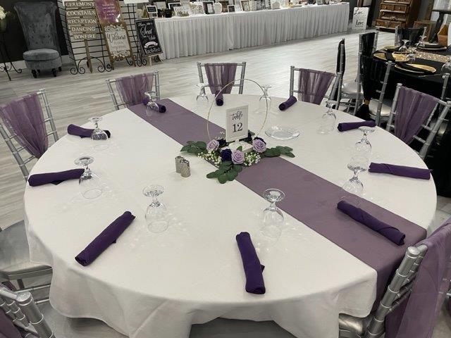 A round table with purple napkins and white tablecloth.