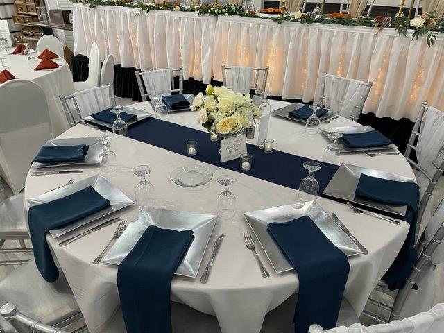 A round table with blue napkins and white linens.