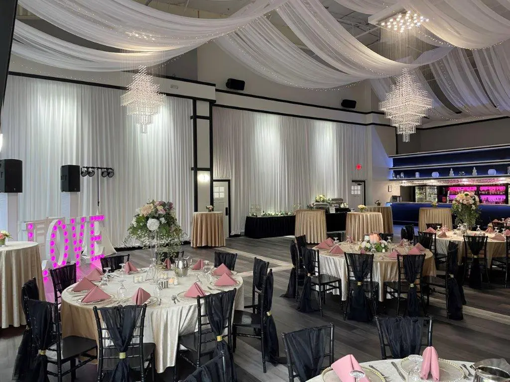 A banquet hall with tables and chairs, chandeliers and pink decorations.