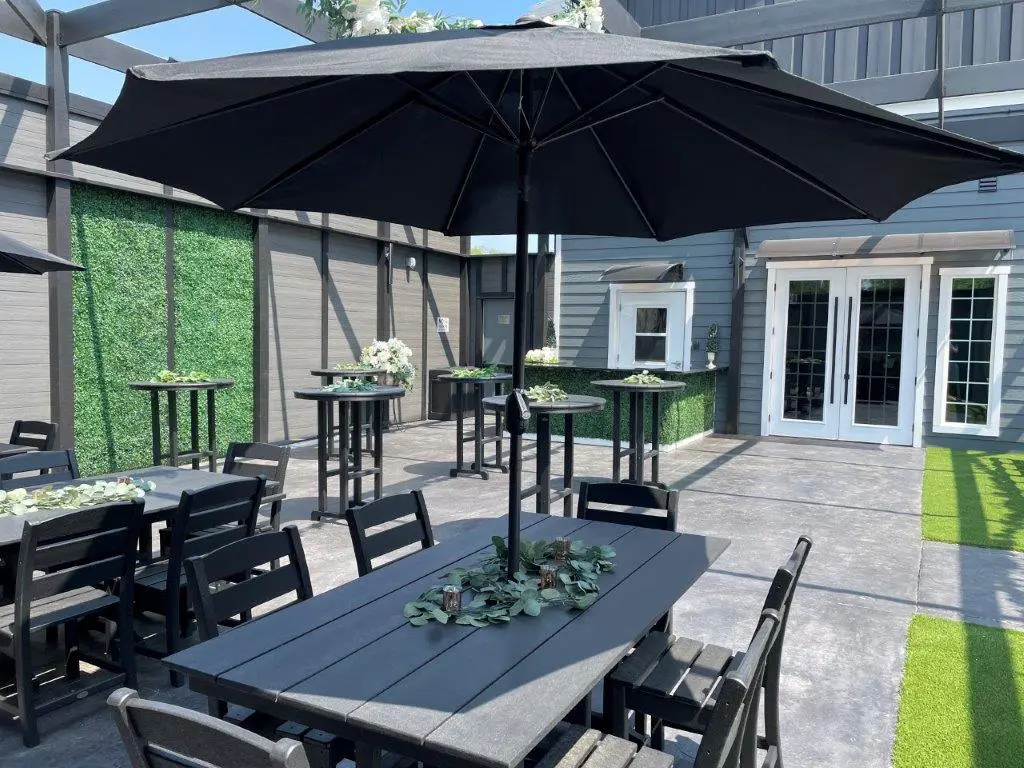 A patio with tables and chairs, an umbrella and a door.