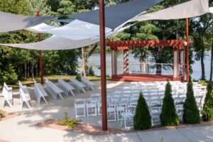 A large outdoor wedding with white chairs and blue umbrellas.