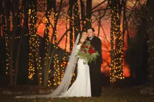 A bride and groom pose for the camera in front of trees.