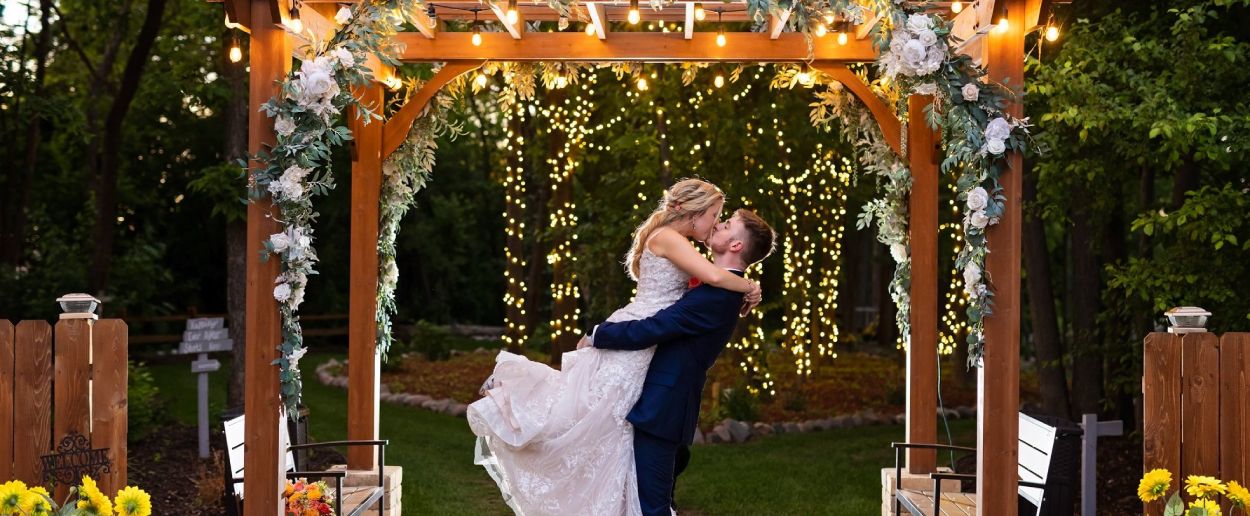 A bride and groom are dancing under the arbor.