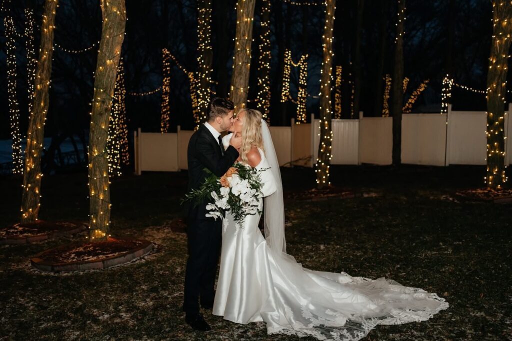 Newlyweds kissing outside under the tree lights